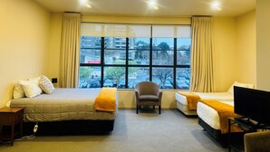 Een hotelkamer met twee bedden, een stoel, een televisie en een groot raam met uitzicht op de stad.