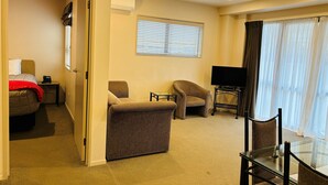 Een hotelkamer met een bed, twee fauteuils, een glazen tafeltje, een televisie en een raam met jaloezieën.