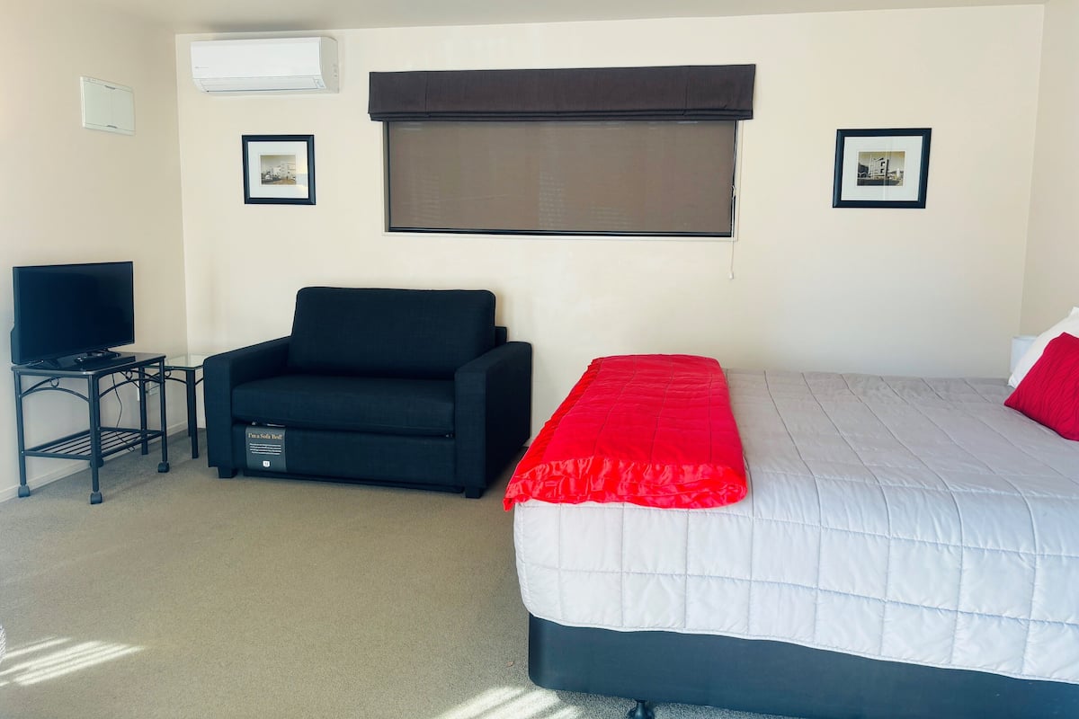A hotel room with a bed, a sofa, a TV on a small table, and two framed pictures on the wall.