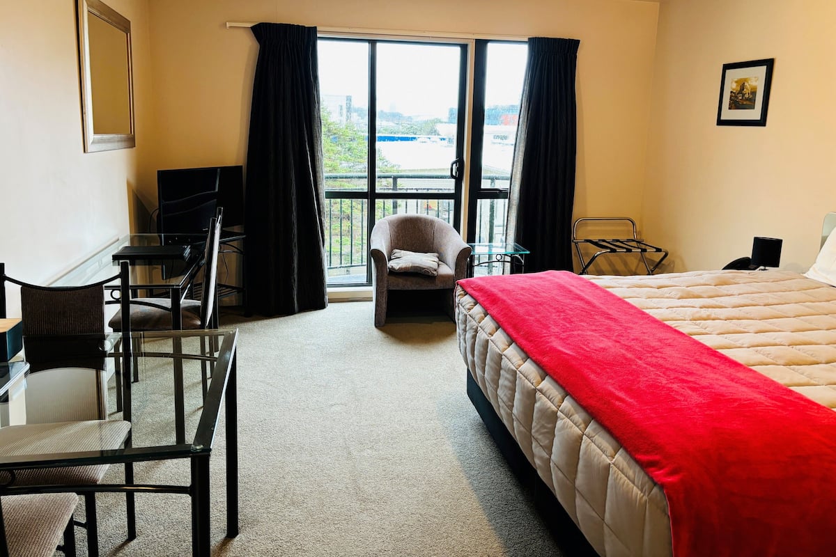 A hotel room with a bed, a desk, a chair, and a balcony with curtains.
