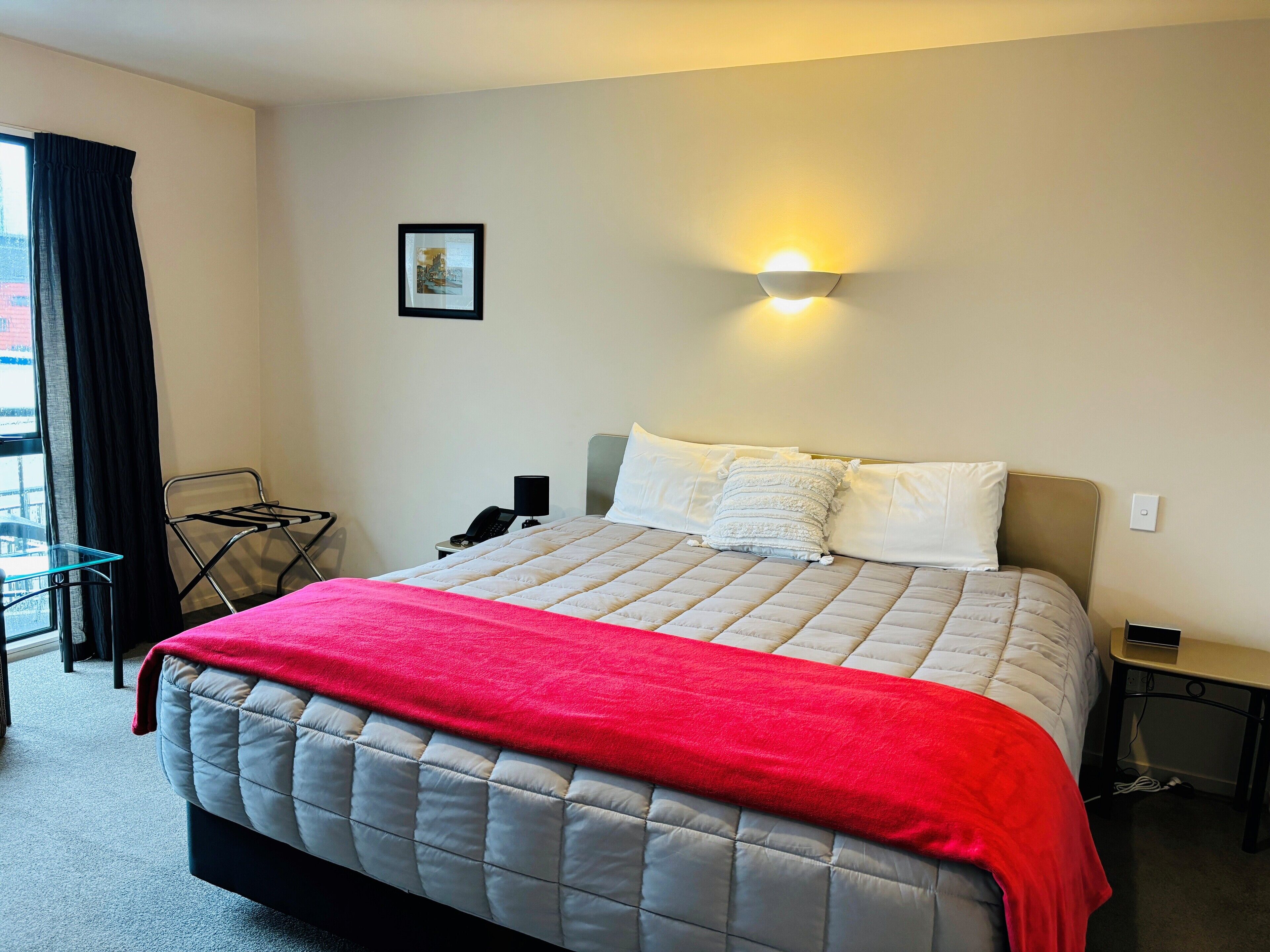 A neatly made bed with a red blanket, a bedside lamp, and a framed picture on the wall.