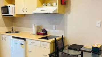 A compact kitchen with a microwave, stove, and refrigerator. There is a dining table with chairs and a fire extinguisher on the wall.