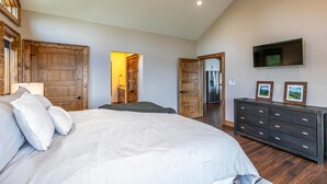 A bedroom with a large bed, wooden doors, a dresser, and a TV on the wall. - Blue Heaven - Long Range Views, Hot Tub, Luxury Home, Near Blowing Rock! (Boone)