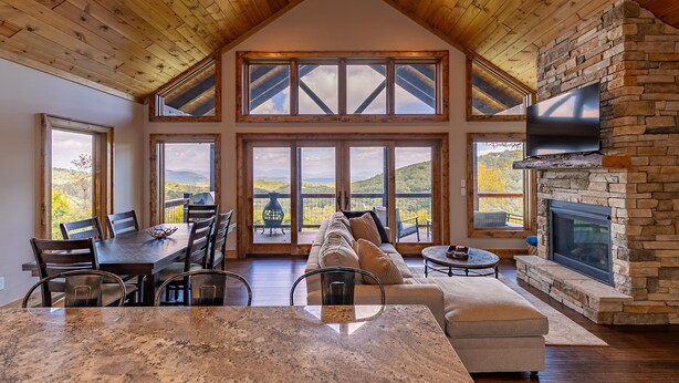 A spacious living area with a high ceiling, large windows, a stone fireplace, and a cozy seating arrangement. - Blue Heaven - Long Range Views, Hot Tub, Luxury Home, Near Blowing Rock! (Boone)