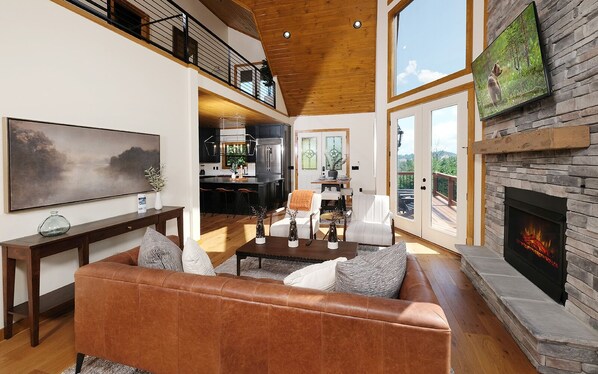 A spacious living room with a leather sofa, a fireplace, and a large window overlooking a deck.