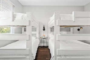 Une chambre avec des lits superposés, une petite table avec une lampe et une fenêtre avec des stores.
