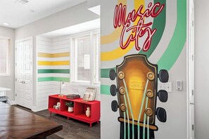 Quarto com parede listrada em vermelho e branco, cabeceira com formato de guitarra e um letreiro que diz 'Music City'.