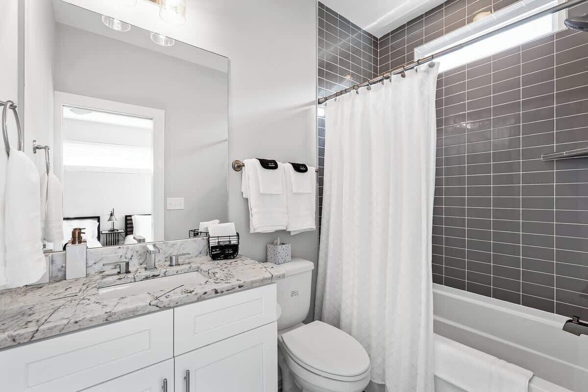 A bathroom with a white toilet, a marble sink, a mirror, and a shower curtain.