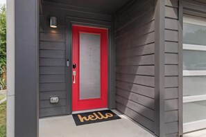 A red door with a glass panel, a mailbox, and a 'hello' mat on a concrete step.