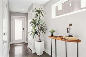A hallway with a white door, a potted plant, a small table with a lamp, and a book.