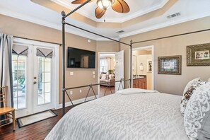 A bedroom with a large bed, a TV, a balcony, and a view of the outside.
