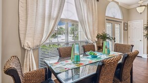 A dining area with a glass table, woven chairs, and a view through large windows. - 🐬Destiny East Luxury Home~Golf Cart~Close to the Beach~Five O'Clock Somewhere🐬 (Destin)