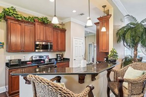 A kitchen with wooden cabinets, a stainless steel microwave, a toaster, and a coffee maker. There are wicker chairs and a large potted plant.