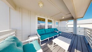 Eine überdachte Terrasse mit weißer Geländer, einem Türkis-Sofa und einem kleinen Tisch.
