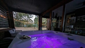 A hot tub with a purple light, surrounded by wooden furniture and a glass enclosure. - Luxe | Hot Tub | Firepit | Heat Floors | EV | Walk2Matthews (Matthews)