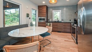 A modern kitchen with a round marble table, wooden flooring, and stainless steel appliances. - Luxe | Hot Tub | Firepit | Heat Floors | EV | Walk2Matthews (Matthews)