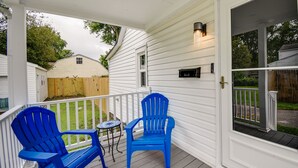 Eine überdachte Veranda mit zwei blauen Adirondack-Stühlen, einem kleinen runden Tisch und einem Briefkasten.