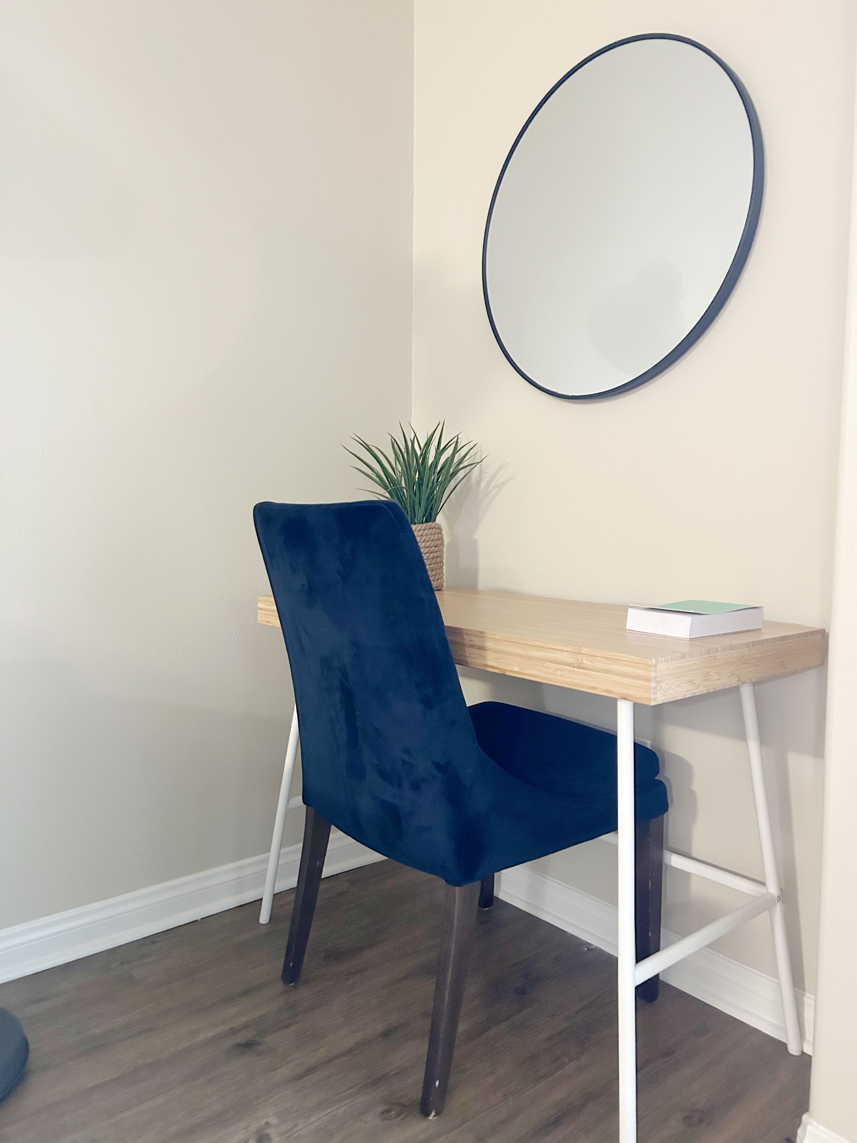 Habitación de esquina con escritorio, silla y un espejo redondo en la pared.