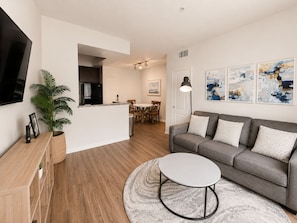 A modern living room with a grey sofa, a round coffee table, and a TV on the wall. - Sunnyside Up! Gorgeous Pool View with Balcony (Marina del Rey)