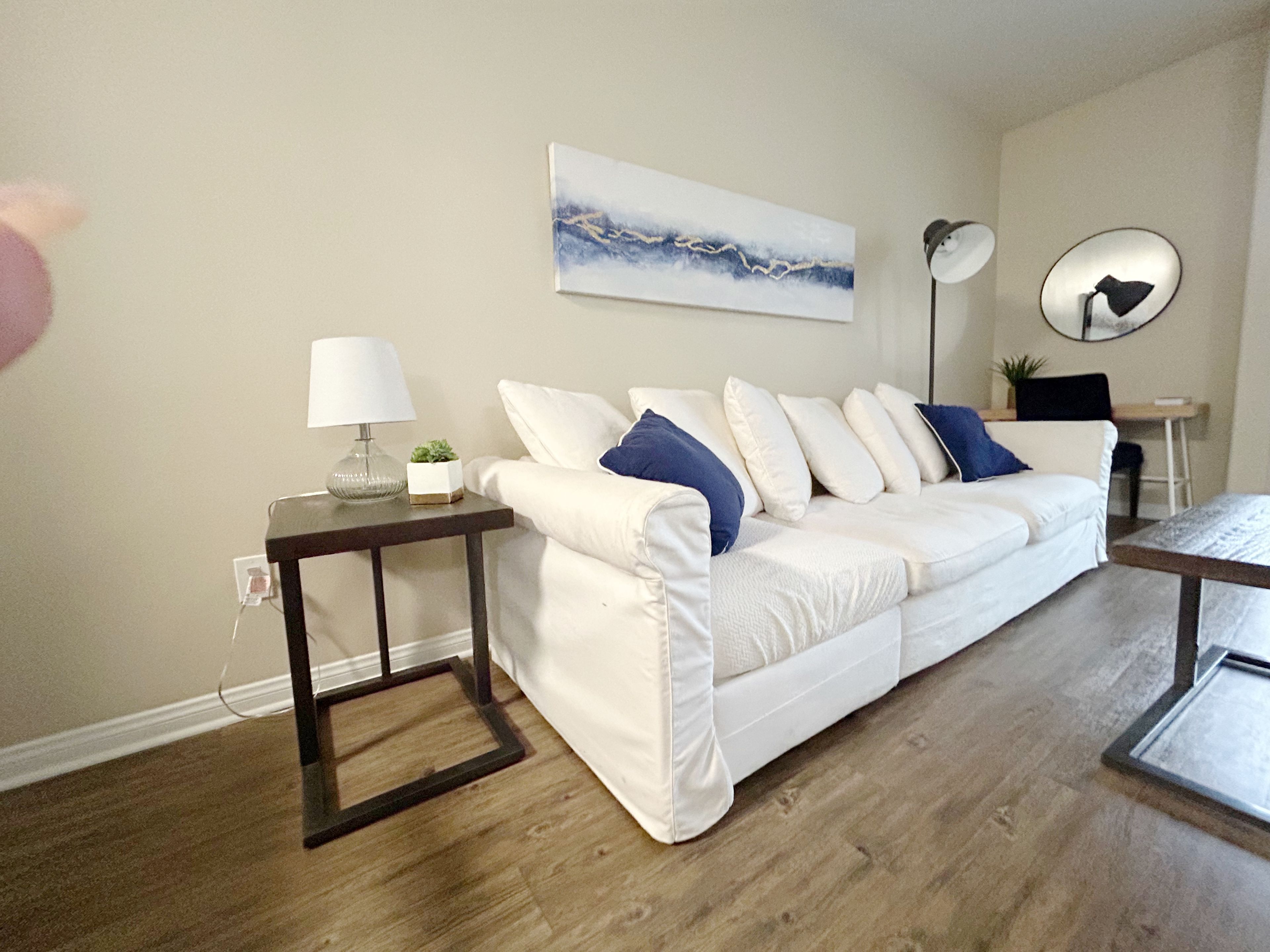 Un salon moderne avec un canapé blanc, une table d’appoint avec une lampe, une table basse et un tableau accroché au mur.