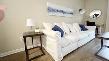A modern living room with a white sofa, a side table with a lamp, a coffee table, and a painting on the wall.