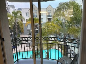 Un balcón con vista a una piscina, rodeado de vegetación y edificios residenciales.