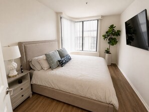 Een slaapkamer met een bed, nachtkastje, lamp en een raam met jaloezieën.