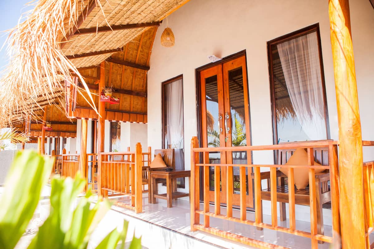 A wooden veranda with a thatched roof, wooden chairs, and a glass door leading to a room.