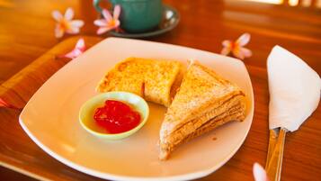 A plate with two sandwiches and a small bowl of ketchup, a green cup, and a white napkin on a wooden table.
