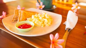A plate of scrambled eggs, toast, and a small bowl of ketchup on a wooden table. - Dayuh House (Penida Island)