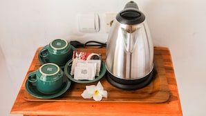 A wooden tray with a stainless steel coffee pot, two green cups, a plate with sugar packets, and a white flower. - Dayuh House (Penida Island)