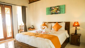 A hotel room with a wooden bed, a nightstand with a lamp, a painting on the wall, and a view through a door. - Dayuh House (Penida Island)