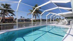 Una piscina con cubierta blanca, rodeada de palmeras y casas.