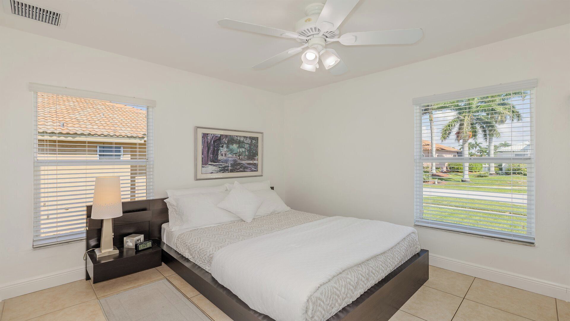 A bedroom with a bed, a nightstand, a ceiling fan, and two windows with blinds.