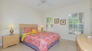 A bedroom with a bed, two bedside tables, a nightstand, a ceiling fan, and a window with blinds.