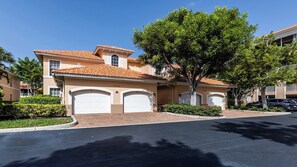 A two-story house with a tiled roof, two garage doors, and a large tree in front.