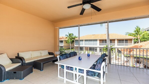 A sunlit patio with a white table and chairs, a sofa, and a ceiling fan.