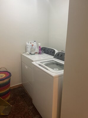 A compact laundry area with a front-loading washing machine, a dryer, and a small shelf with cleaning supplies.