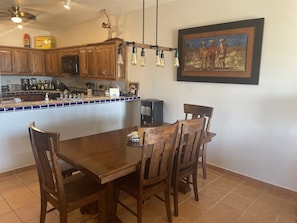 A dining area with a wooden table and chairs, a kitchen with wooden cabinets and a tiled backsplash, and a ceiling fan.
