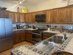 A kitchen with wooden cabinets, a stainless steel refrigerator, a microwave, a stove, and a sink with a tiled backsplash.