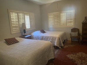 A bedroom with two beds, a nightstand with a lamp, a chair, and a window with blinds.