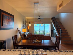 A dining area with a wooden table, chairs, and a view of the ocean through large windows.
