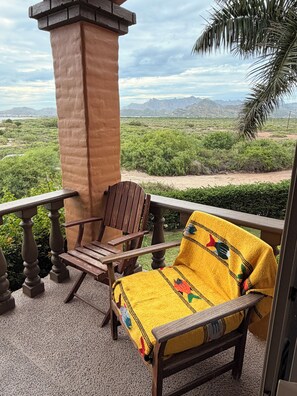 A balcony with a wooden chair and a yellow blanket, overlooking a mountainous landscape.