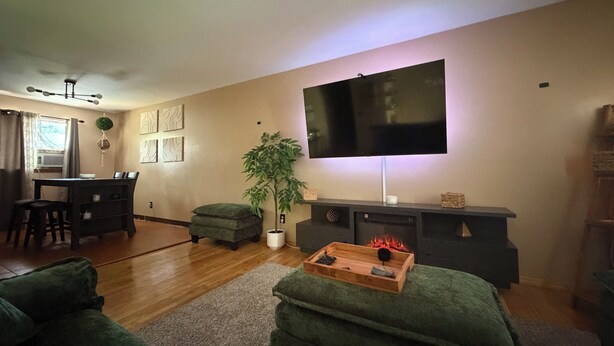 Una sala de estar con un televisor de pantalla plana, un comedor con mesa y sillas, y un sofá verde.