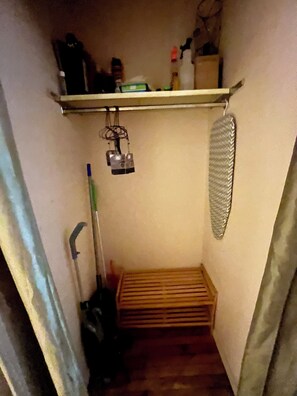 A narrow hallway with a wooden bench, a hanging shower curtain, and a shelf with various items.