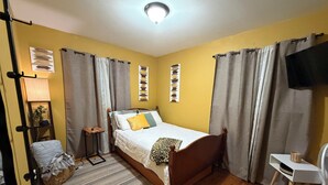 Un dormitorio con cama, mesita de noche, lámpara, silla y televisor.