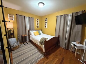A bedroom with a bed, a bedside table, a lamp, a chair, and a television.