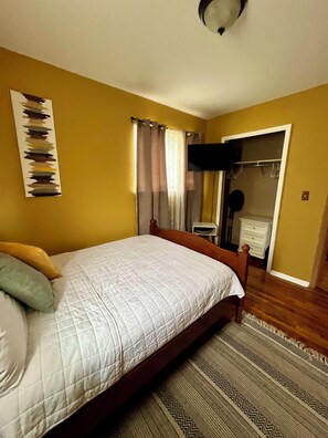 A bedroom with a bed, a wardrobe, a television, and a patterned rug.
