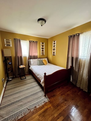 Une chambre à coucher avec un lit en bois, une lampe sur pied, une table de chevet, un tapis à motifs et un ventilateur de plafond.