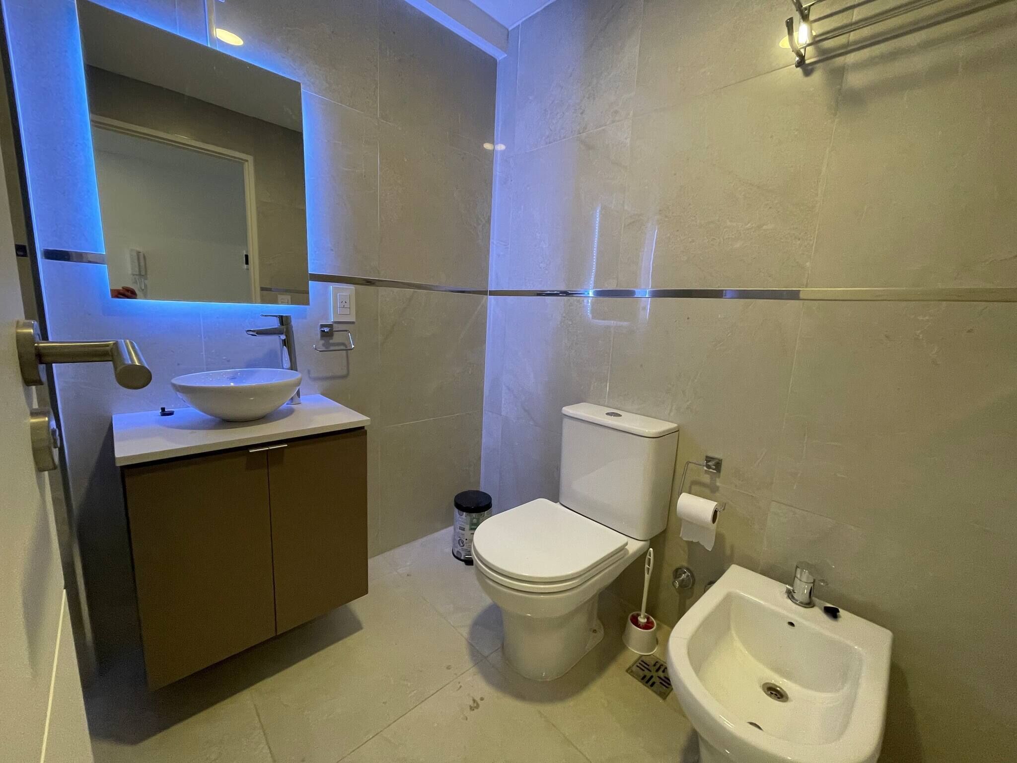 A modern bathroom with a vessel sink, toilet, bidet, and a small pedestal sink.
